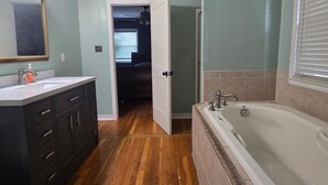 A bathroom with a wooden floor, a large bathtub, a vanity with a mirror, and a toilet. -  A 3-bedroom house  in Georgetown, close to downtown, fully fenced back yard.  (Georgetown)