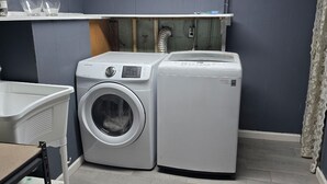 A laundry room with two washing machines, a drying machine, a shelf with glass jars, and a white sink. -  A 3-bedroom house  in Georgetown, close to downtown, fully fenced back yard.  (Georgetown)