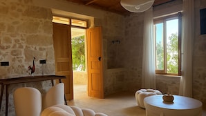 Una habitación acogedora con pared de piedra, una puerta de madera que da al exterior, un sofá blanco, una mesita redonda pequeña y una lámpara en el techo.