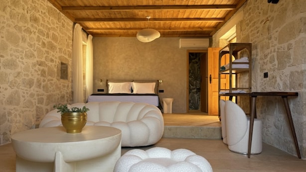 Un dormitorio acogedor con pared de piedra, techo de madera, cama y una pequeña zona de estar con mesa y sillas.