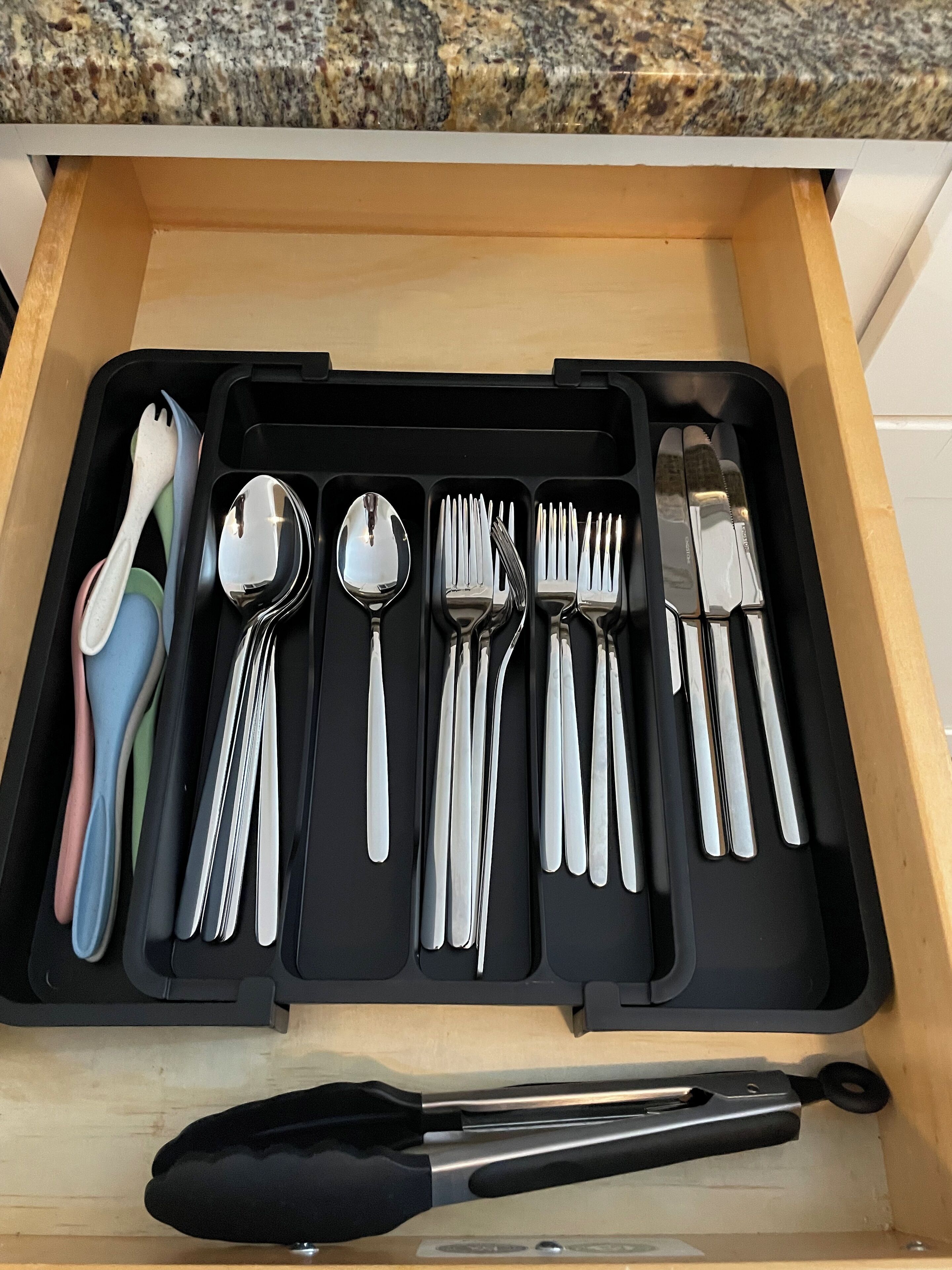Eine Schublade mit einer schwarzen Ablage, auf der verschiedene Besteckteile wie Löffel, Gabeln und Messer liegen.
