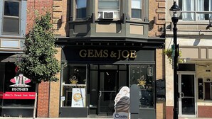 A corner building with a storefront named "Gems & Joe" featuring a large sign and a black awning.