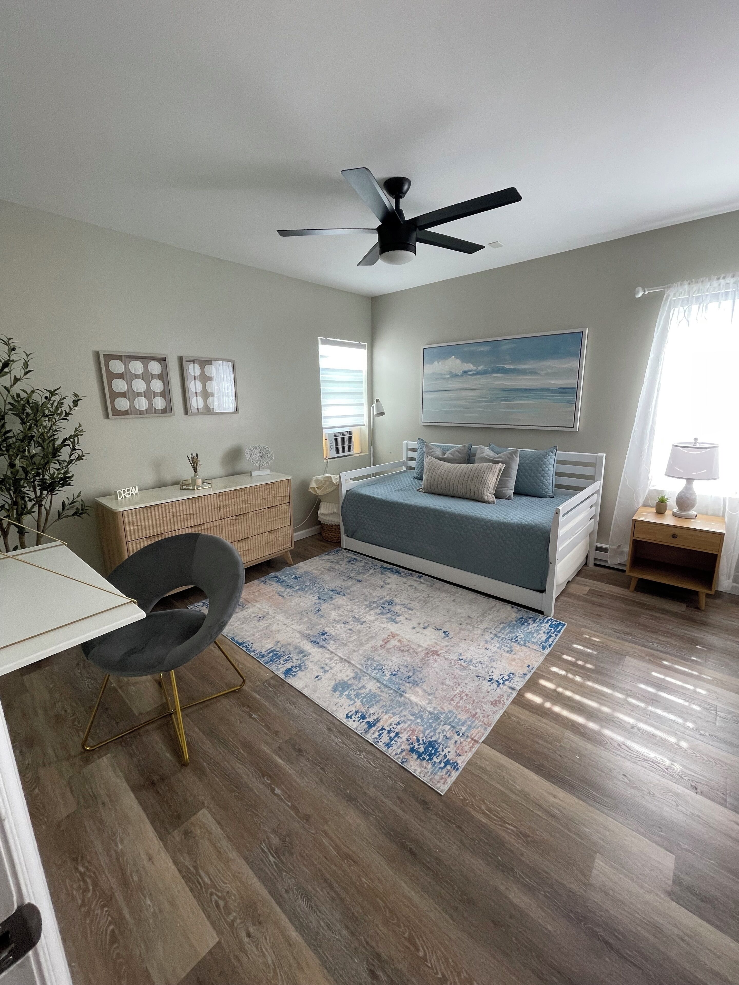 A bedroom with a bed, desk, chair, and a ceiling fan.