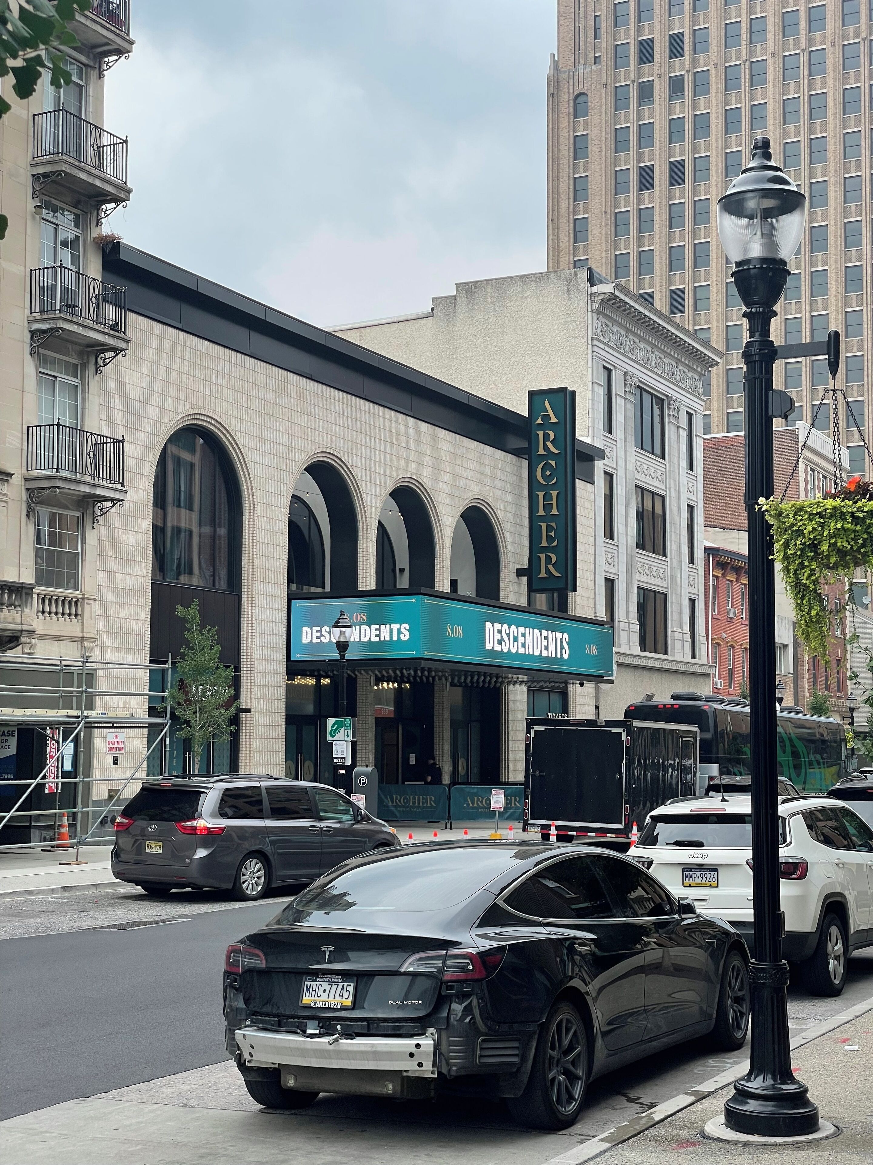 A building with a sign reading 'ARCHER DESCENDENTS' and a black car parked in front.