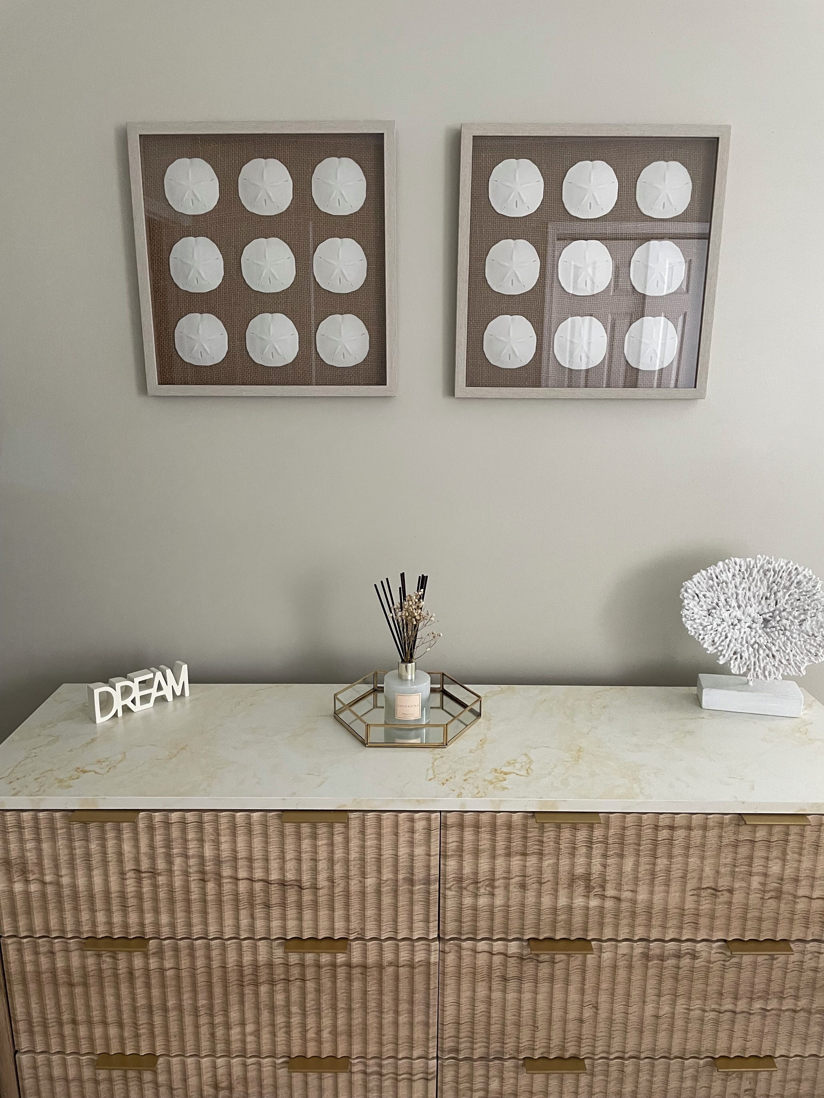A marble-top table with a glass centerpiece holding a bottle and reed diffuser. Above the table, there are two framed artworks with circular patterns.