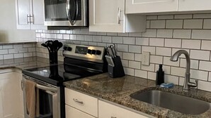 A modern kitchen with white cabinets, stainless steel appliances, a granite countertop, and a built-in sink.