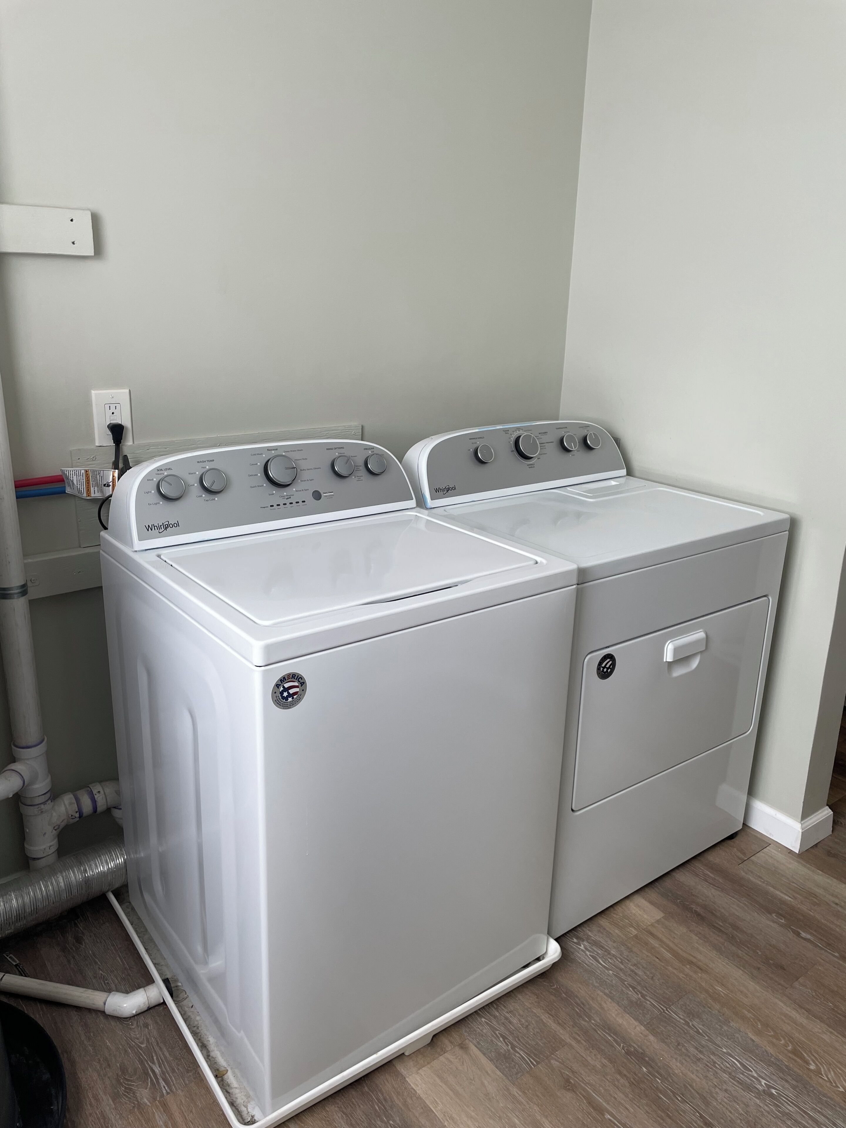 A laundry room with two stacked front-loading washers and dryers, a power outlet, and a water pipe.