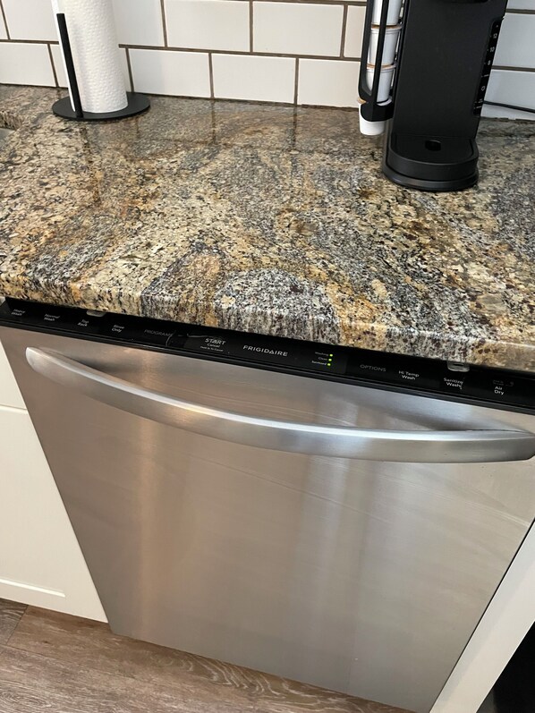 Un lavavajillas de acero inoxidable con un panel de control que muestra opciones como “Iniciar”, “Limpiar” y “Sanitizar”.