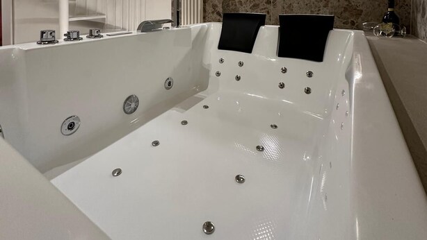 Een moderne badkamer met een groot bad, een witte spiraaltrap en een muur met een steenmotief.