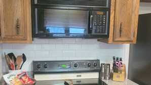 Una cocina con armarios de madera, un microondas negro, una estufa y un refrigerador.