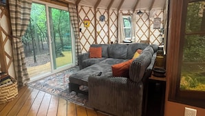 Un salon chaleureux avec un grand canapé, une petite table et une fenêtre donnant sur une forêt.
