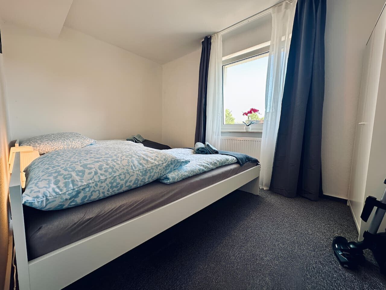 A small, single-bed room with a window, curtains, and a radiator.