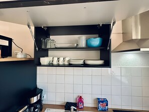 A kitchen with white tiled backsplash, black shelves holding plates, cups, and a blue bowl.