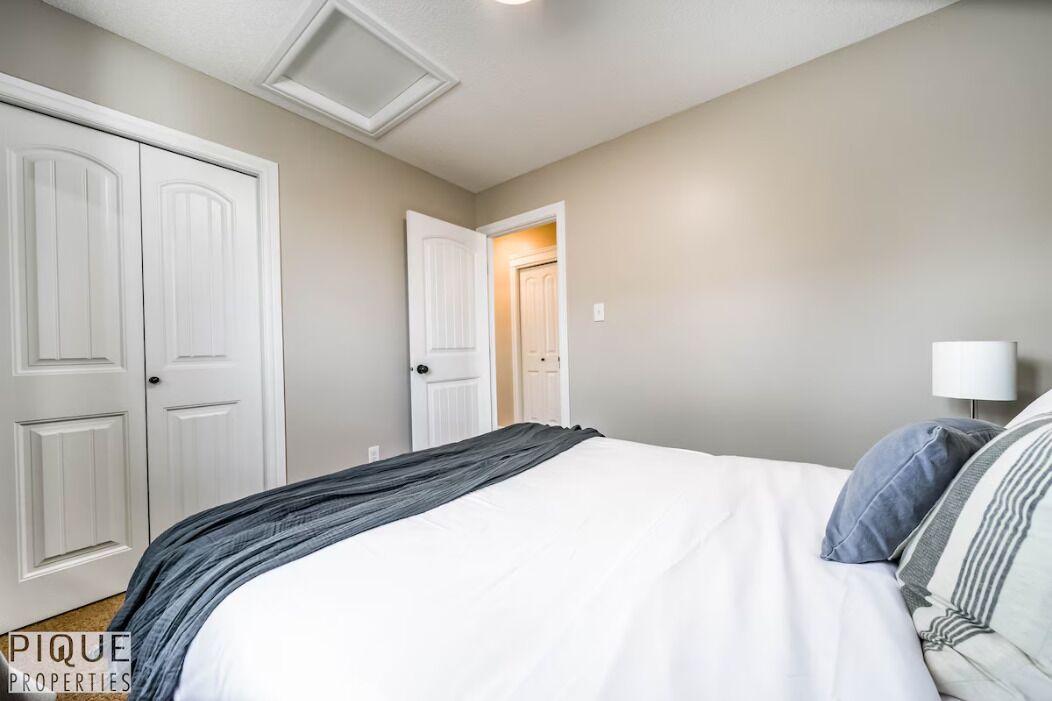 A bedroom with a large bed, two white doors, and a nightstand with a lamp.