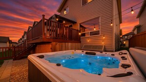 A hot tub in a backyard with a wooden deck and string lights. - 5BD Jungle Oasis - Hot Tub - BBQ - King Bed - Games - AC (Edmonton)
