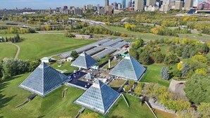 A large solar farm with multiple triangular solar panels, surrounded by green fields and trees, with a city skyline in the background. - 5BD Jungle Oasis - Hot Tub - BBQ - King Bed - Games - AC (Edmonton)