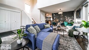 A modern living room with a blue sofa, a coffee table, and a staircase leading to another level. - 5BD Jungle Oasis - Hot Tub - BBQ - King Bed - Games - AC (Edmonton)