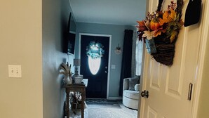 Un couloir doté d’un sol recouvert de moquette, une porte ornée d’une guirlande et une petite table sur laquelle se trouvent une lampe et des objets décoratifs.