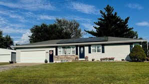 Une maison de plain-pied avec un garage, un porche à l’avant et un petit jardin devant.