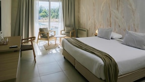 Ein Hotelzimmer mit einem großen Bett, einem Schreibtisch mit Stuhl, einem kleinen Tisch und Blick ins Freie.