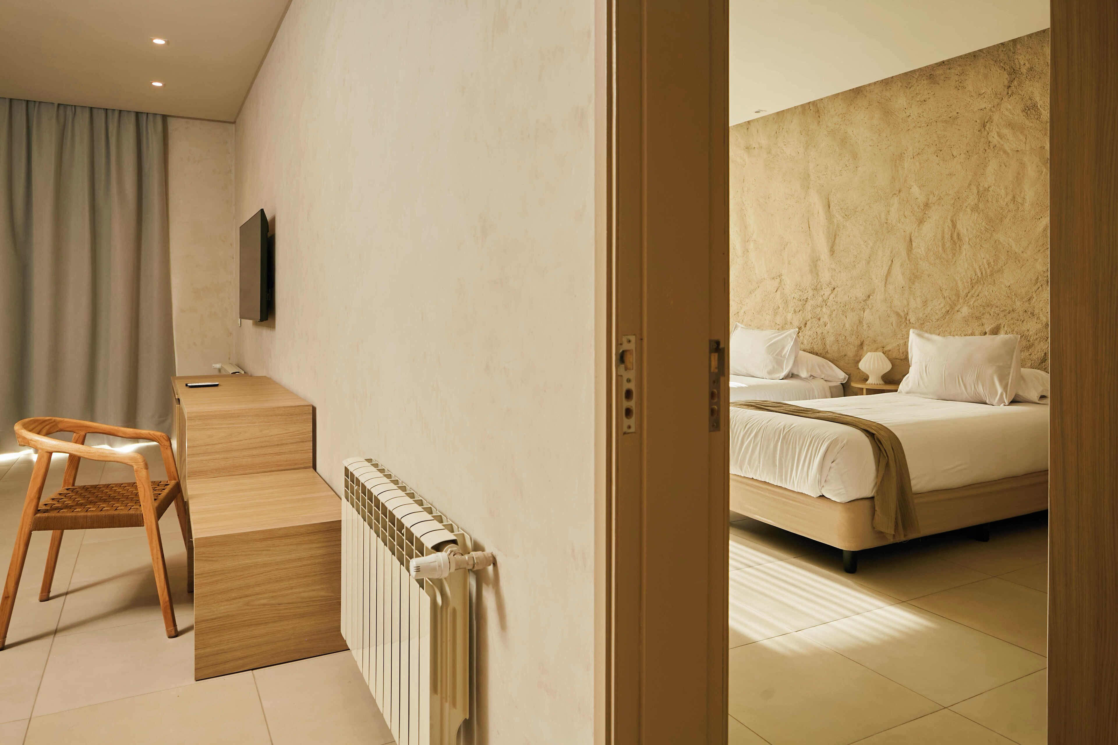A hotel room with a wooden desk, a chair, a bed with white bedding, and a television mounted on the wall.