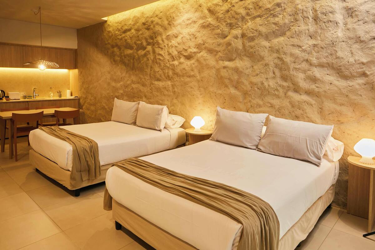 A hotel room with two beds, a small desk, and a kitchenette.