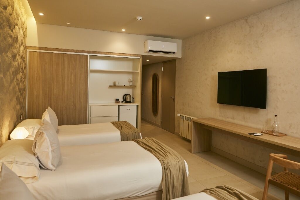 A hotel room with two beds, a TV, a desk, a wardrobe, and a kitchenette.