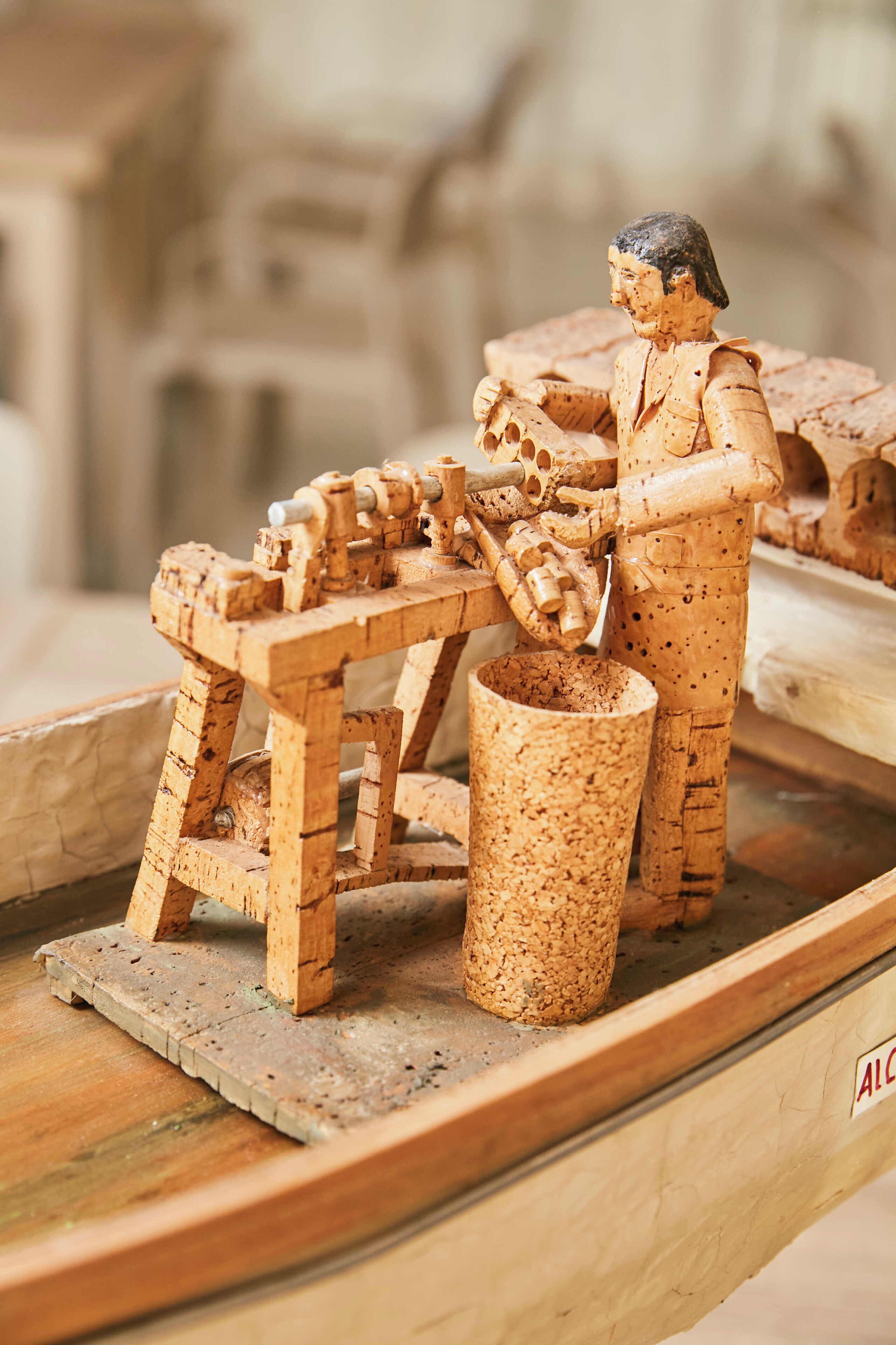 Eine Holzskulptur, die eine Person bei der Arbeit mit Werkzeugen an einem Tisch zeigt.