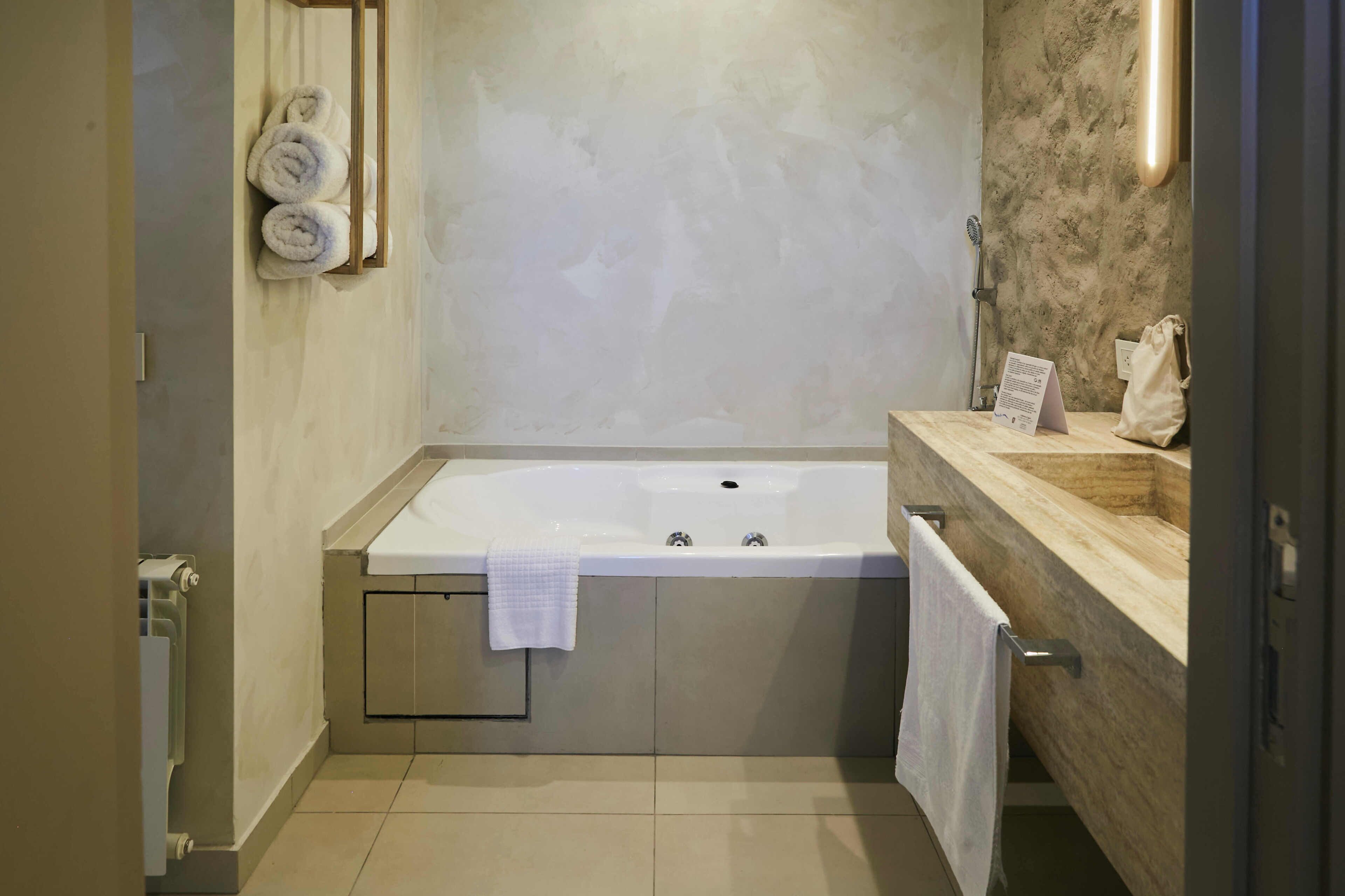 Un baño moderno con una bañera grande, tocador de madera y toallas en la pared.