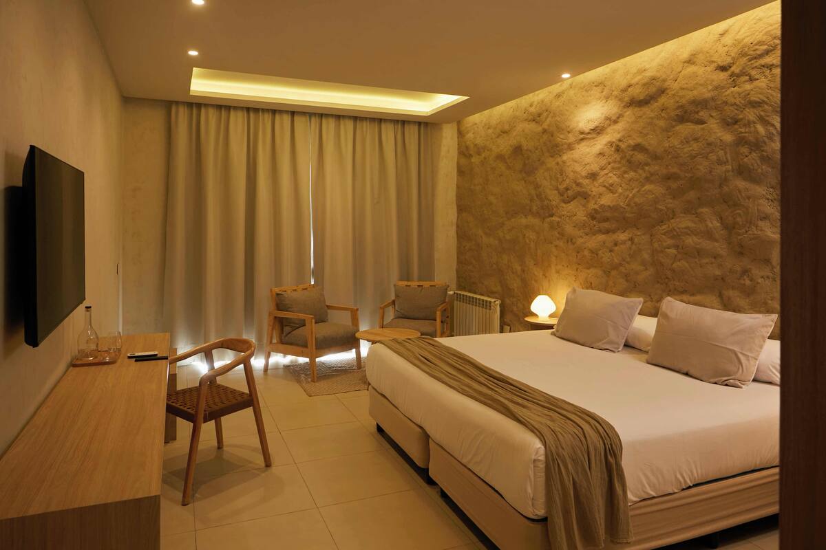 A modern hotel room with a large bed, a desk, a chair, and a television.