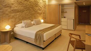A bedroom with a bed, bedside lamps, a wooden wardrobe, and a small kitchenette.