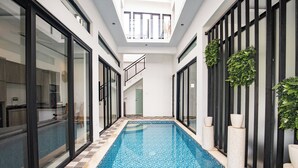 A modern indoor swimming pool with glass walls and a tiled floor, surrounded by a minimalist interior with black railings and potted plants. - Triple Heaven Canggu (Canggu)