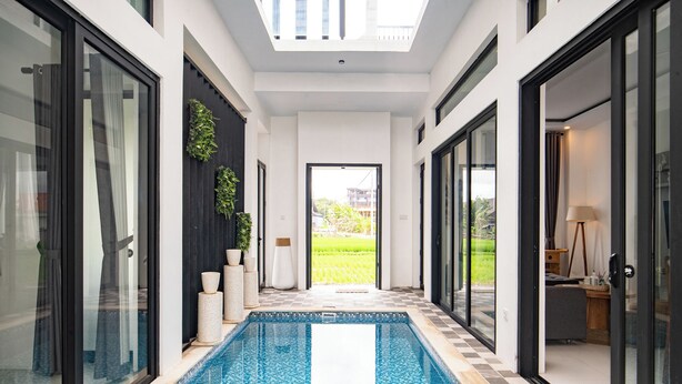 A modern indoor swimming pool with a tiled floor, surrounded by glass doors and windows, leading to a view of a green landscape. - Triple Heaven Canggu (Canggu)
