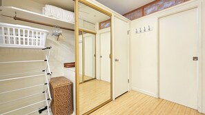 Un dressing accessible sans porte, avec une porte de placard miroir, un panier à linge blanc et un tabouret en osier.