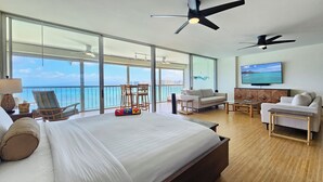 A hotel room with a large bed, a sofa, a TV, and a balcony with a view of the ocean. - 11th Floor King Bed Beachfront Condo at Sans Souci (Honolulu)