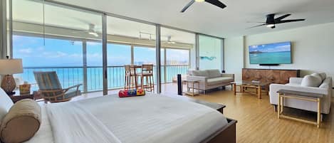 A hotel room with a large bed, a sofa, a TV, and a balcony with a view of the ocean.