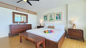 Habitación de hotel con una cama grande, un banco de madera, un aparador, una mesita de noche con lámpara y tres cuadros en la pared.