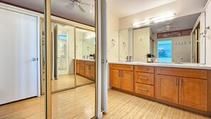 A bathroom with wooden cabinets, a large mirror, and a ceiling fan. - 11th Floor King Bed Beachfront Condo at Sans Souci (Honolulu)