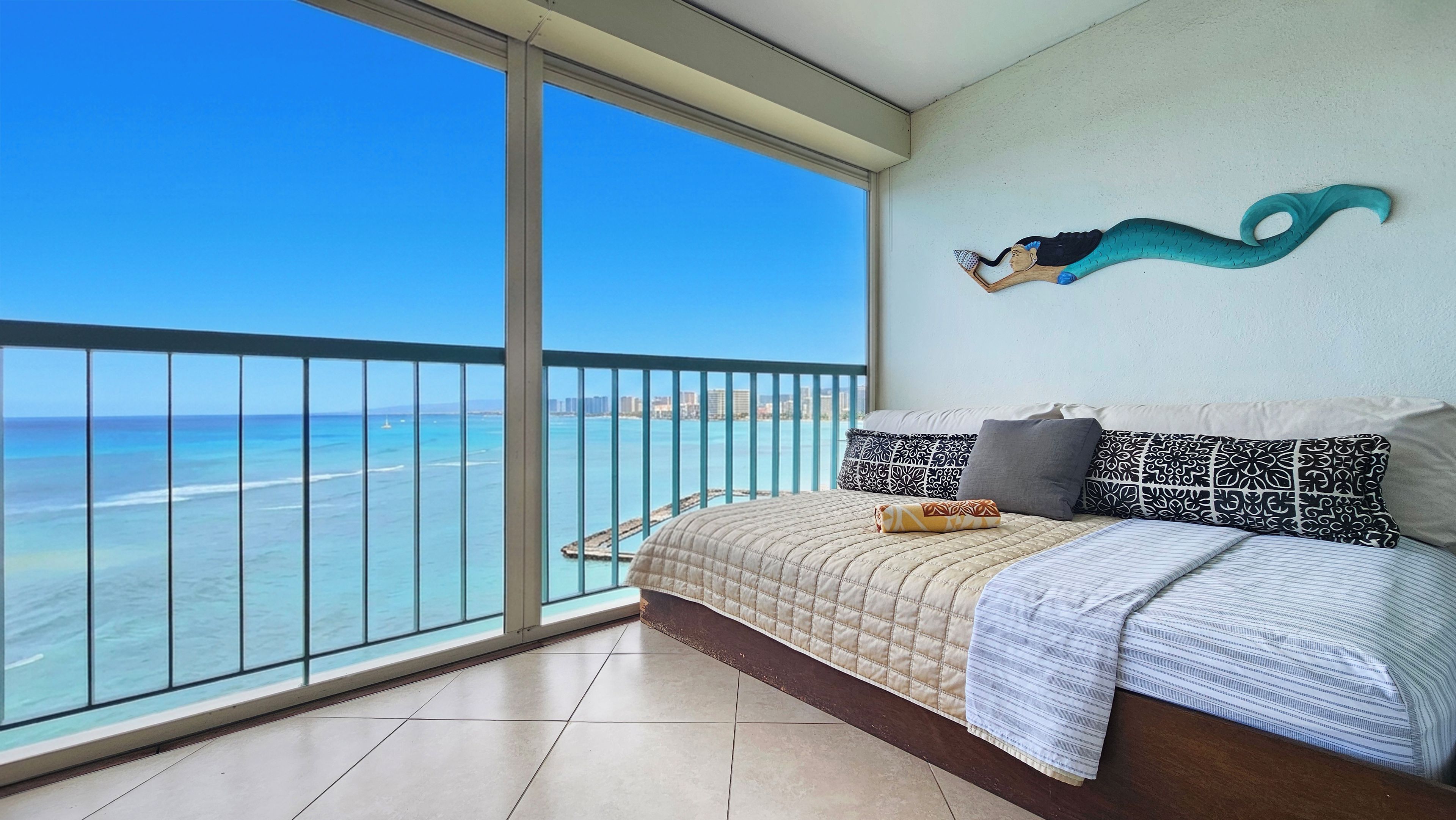A balcony with a view of the ocean and a bed with patterned pillows.