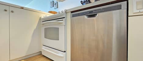 Una cocina con horno blanco, lavavajillas de acero inoxidable y armarios de madera.
