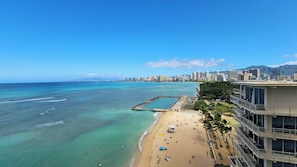 Una playa con aguas turquesas cristalinas, una orilla de arena y un horizonte urbano al fondo.