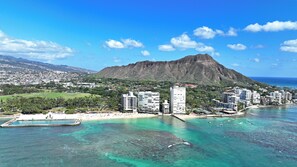 A coastal cityscape with a prominent mountain, clear turquoise waters, and a beach area. - 11th Floor King Bed Beachfront Condo at Sans Souci (Honolulu)