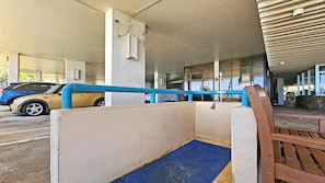 Entrada de un estacionamiento con barandilla azul, pared de concreto y felpudo azul que conduce a un banco de madera.