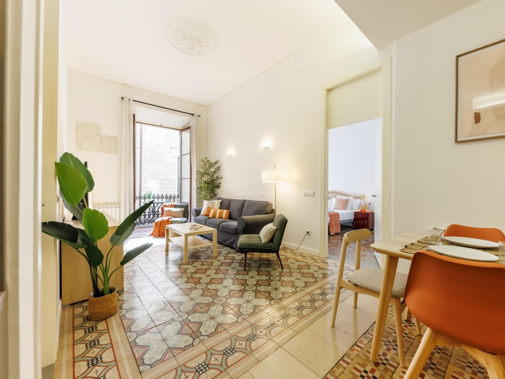 Una sala de estar moderna con sofá, mesa de centro y comedor. Hay un ventanal y una puerta que da a otra habitación.