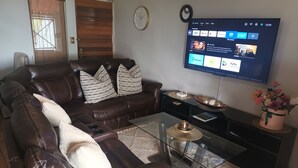 A living room with a brown leather sofa, a glass coffee table, a flat-screen TV, and a decorative flower arrangement.