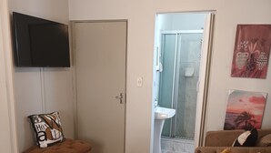 A bedroom with a bed, a television, a door, and a bathroom visible through an open door.