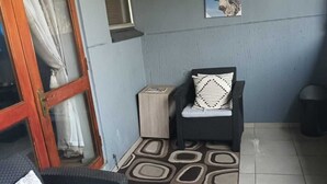 A small, enclosed balcony with a wicker chair, a small table, and a patterned rug.