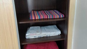 A wooden wardrobe with three shelves; the top shelf has a colorful striped pillow, the middle shelf has folded clothes, and the bottom shelf has a red towel. - Modern Casablanca Apartment – Parking, A/C & WiFi (Casablanca)