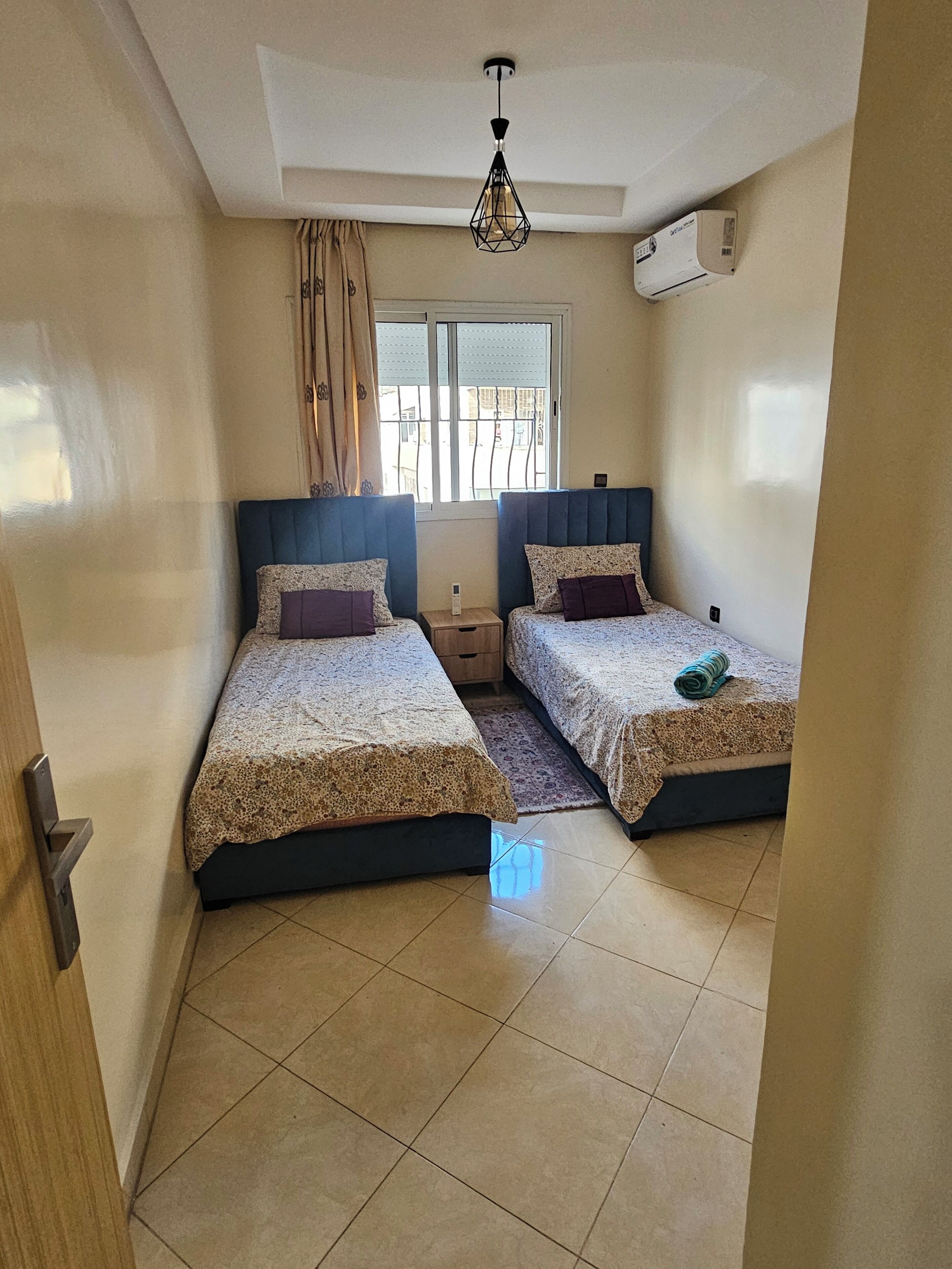 Un dormitorio con dos camas, una ventana con cortinas, una lámpara de techo y un equipo de aire acondicionado.