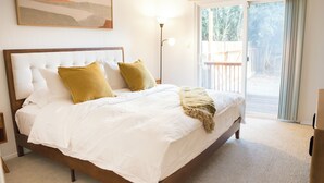 A bedroom with a large bed, white bedding, and a view of the outdoors through a sliding glass door.